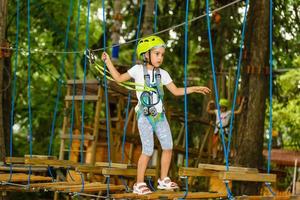 ragazza felice della scuola che gode dell'attività in un parco di avventura di arrampicata in una giornata estiva foto