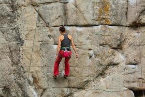 un' giovane donna con un' corda impegnato nel il gli sport di roccia arrampicata su il roccia. foto