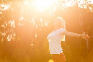 bellezza ragazza all'aperto godendo natura. bellissimo adolescenziale modello ragazza nel bianca vestito in esecuzione su il primavera campo, raccolta mani nel sole luce. foto