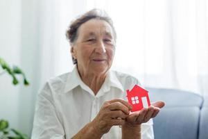 anziano donna detiene il disposizione di il Casa nel sua mani foto