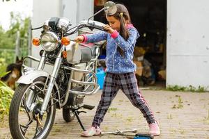 poco ragazza riparazione un' motociclo, alunno ragazza nel motocicletta meccanica foto
