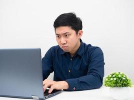 asiatico uomo intento per Lavorando a partire dal casa con il suo il computer portatile su il tavolo foto