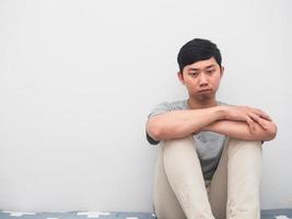 giovane uomo sedersi su il letto abbracciare ginocchio riflessivo tristezza emozione bianca sfondo foto