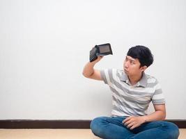 asiatico uomo seduta su pavimento guardare a vuoto portafoglio no i soldi si sente scoraggiato foto