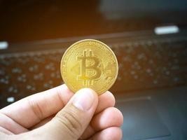 mano Tenere oro bitcoin davanti di il computer portatile sfondo foto