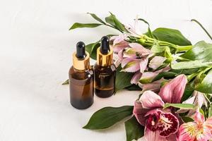 Due cosmetico bottiglie con un' contagocce su un' bianca sfondo con un' mazzo di alstroemeria fiori. alla moda naturale Prodotto per giovane pelle. foto