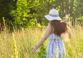 giovane donna raccolta fiori nel il prato nel estate sera foto