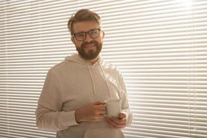 giovane elegante uomo con barba sta e sorridente. concetto di godendo il mattina sole e positività foto