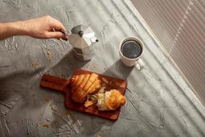 prima colazione con brioche su taglio tavola e nero caffè. mattina pasto e prima colazione concetto. foto