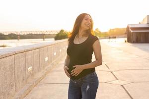 ritratto di ispanico incinta donna a piedi su argine a tramonto. gravidanza e maternità concetto. foto