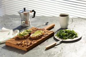 affettato avocado su crostini pane con noccioline e caffè. spinaci su un' piatto e moka pentola. prima colazione e salutare cibo concetto. foto