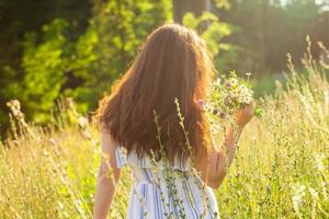 posteriore Visualizza di bellissimo giovane donna a piedi tra fiori selvatici su soleggiato estate giorno. concetto di il gioia di comunicare con estate natura foto