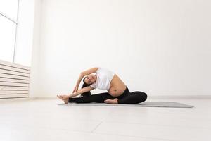 intenzionale incinta donna esercizi durante yoga classe e rilassa mentre seduta su un' stuoia su il pavimento. concetto di fisico e mentale preparazione di il corpo per parto. posto per testo foto