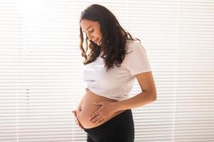 sorridente giovane bellissimo incinta donna toccante sua pancia e gioire. concetto di positivo e piacevole sentimenti mentre in attesa per il bambino foto