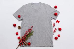 vicino su grigio vuoto modello t camicia con copia spazio e Natale vacanza concetto. superiore Visualizza modello maglietta e rosso vacanze decorazioni su bianca sfondo. contento nuovo anno Accessori. natale attrezzatura foto