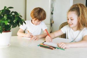 Due fratelli fratello e sorella bambino piccolo ragazzo gemello ragazza disegno su tavolo nel cucina a casa foto