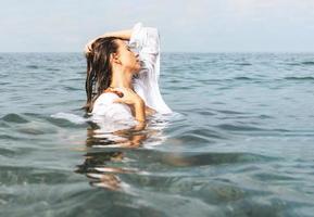 moda bellezza ritratto di giovane bellissimo donna con lungo capelli e bianca camicia nel il mare. unità con natura, naturale cosmetici, profumi foto