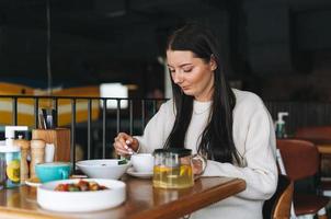 attraente giovane brunetta sorridente donna nel casuale avendo brunch nel il bar, salutare cibo foto