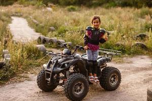 il poco ragazza cavalcate un' quadrilatero bicicletta atv. un' mini quadrilatero bicicletta è un' freddo ragazza nel un' casco e protettivo vestiario. elettrico quadrilatero bicicletta elettrico auto per bambini rende popolare verde tecnologia. foto