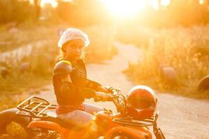 il poco ragazza cavalcate un' quadrilatero bicicletta atv. un' mini quadrilatero bicicletta è un' freddo ragazza nel un' casco e protettivo vestiario. elettrico quadrilatero bicicletta elettrico auto per bambini rende popolare verde tecnologia. foto