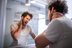 ritratto di assonnato giovane uomo sbadigli e guardare a specchio nel bagno nel mattina, lato Visualizza. provando per scia su. mancanza di dormire, insonnia e stressante stile di vita. postumi della sbornia. depressione. foto