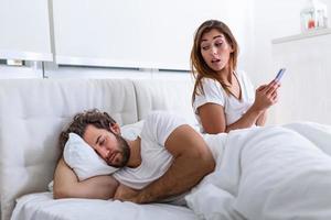 imbrogliare moglie utilizzando mobile Telefono dire bugie nel letto Il prossimo per il suo addormentato marito. affare. imbrogliare fidanzata chat su Telefono mentre fidanzato addormentato nel Camera da letto a notte. selettivo messa a fuoco. foto