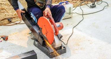 il lavoratore nel il opera Abiti usi un elettrico acciaio taglierina. taglio grande acciaio barre a il costruzione luogo foto