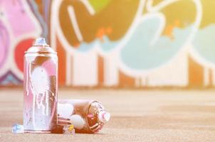 parecchi Usato spray lattine con rosa e bianca dipingere e caps per spruzzatura dipingere sotto pressione è bugie su il asfalto vicino il dipinto parete nel colorato graffiti disegni foto
