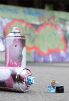 parecchi Usato spray lattine con rosa e bianca dipingere e caps per spruzzatura dipingere sotto pressione è bugie su il asfalto vicino il dipinto parete nel colorato graffiti disegni foto