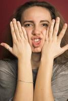 ritratto di emotivo positivo europeo adolescenziale ragazza indossare sua leggero capelli nel panino, urlando nel stupore o stupore conservazione mani su viso foto