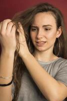 danneggiato capelli. bellissimo triste giovane donna con lungo spettinato capelli. avvicinamento ritratto di femmina modello Tenere disordinato non spazzolato asciutto capelli nel mani. capelli danno, Salute e bellezza concetto. alto risoluzione foto