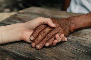 mani di il vecchio uomo e un' donna mano su il legna tavolo nel sole leggero foto