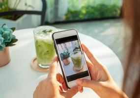 un asiatico donna usi un' smartphone per prendere immagini di verde tè nel un' bar. foto