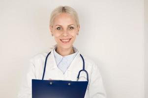 giovane contento femmina medico nel medico cappotto con stetoscopio sorridente con tavoletta nel sua mani foto