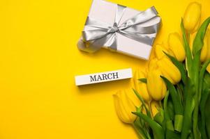 primavera striscione. un' mazzo di giallo tulipani e marzo scritto su un' di legno bloccare. Da donna giorno concetto foto
