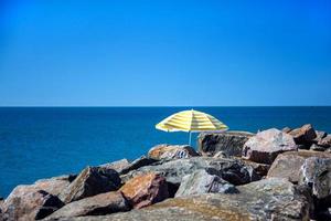 solitario ombrello in piedi nel pietre su un' selvaggio spiaggia foto