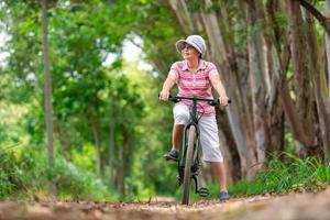 anziano attività commerciale donna, femmina, cavalcata o bicicletta montagna bicicletta nel nazione parco vicino casa cittadina per salutare esercizio nel estate fine settimana foto