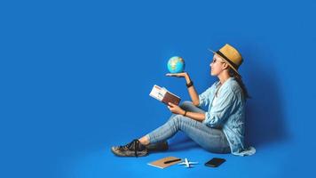 giovane viaggiatore asiatico felice in camicia blu che tiene il passaporto con il mondo della palla in mano. viaggio di concetto con attrezzatura per le vacanze dei viaggiatori, su sfondo blu. viaggiare rilassati foto