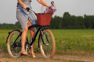 donna nel blu vestito equitazione su un' nero bicicletta nel un' estate campo foto