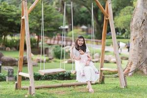 asiatico madre e figlia seduta su swing e sorridente con gioia e felicemente, famiglia caldo e contento bene volte. andando su vacanza nel il giardino parco o ricorrere nel naturale. famiglia attività concetto. foto