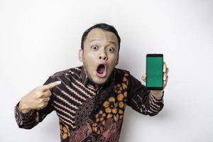 scioccato asiatico uomo indossare batik camicia e mostrando verde schermo su il suo Telefono, isolato di bianca sfondo foto