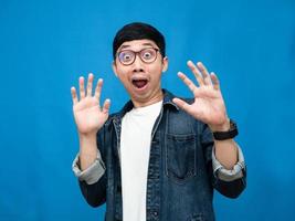 asiatico uomo indossare bicchieri jeans camicia gesto scioccato blu sfondo foto