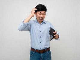 asiatico uomo blu camicia si sente scioccato di no i soldi nel il suo portafoglio si sente sforzo e mal di testa isolato foto