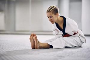 giovane atletico donna con para-abilità allungamento su il pavimento durante taekwondo formazione nel Salute club foto