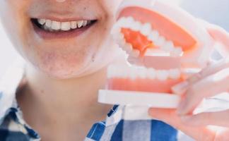 stomatologia concetto, parziale ritratto di ragazza con forte bianca denti guardare a telecamera e sorridente, dita vicino viso. avvicinamento di giovane donna a dal dentista, studio, in casa foto