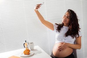 incinta donna assunzione un' se stesso ritratto con sua smartphone mentre prima colazione foto