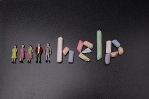 il iscrizione su il Aiuto di colorato gesso accanto persone figurine foto