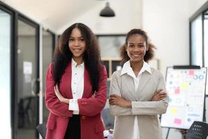 sorridente diverso colleghi donne d'affari Lavorando su il computer portatile insieme, guardare a schermo, In piedi a scrivania nel ufficio, dipendenti discutere progetto strategia, condivisione idee foto