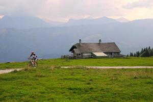 viaggio per sankt-wolfgang, Austria. un' ciclista su il strada fra il i campi con Visualizza su il montagne e un' Casa nel il nuvole. foto