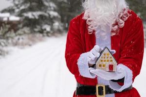 chiave di casa con portachiavi cottage nelle mani di babbo natale all'aperto nella neve. affare per immobili, acquisto, costruzione, trasloco, mutuo. casa accogliente. buon natale, evento di prenotazione di capodanno e sala foto